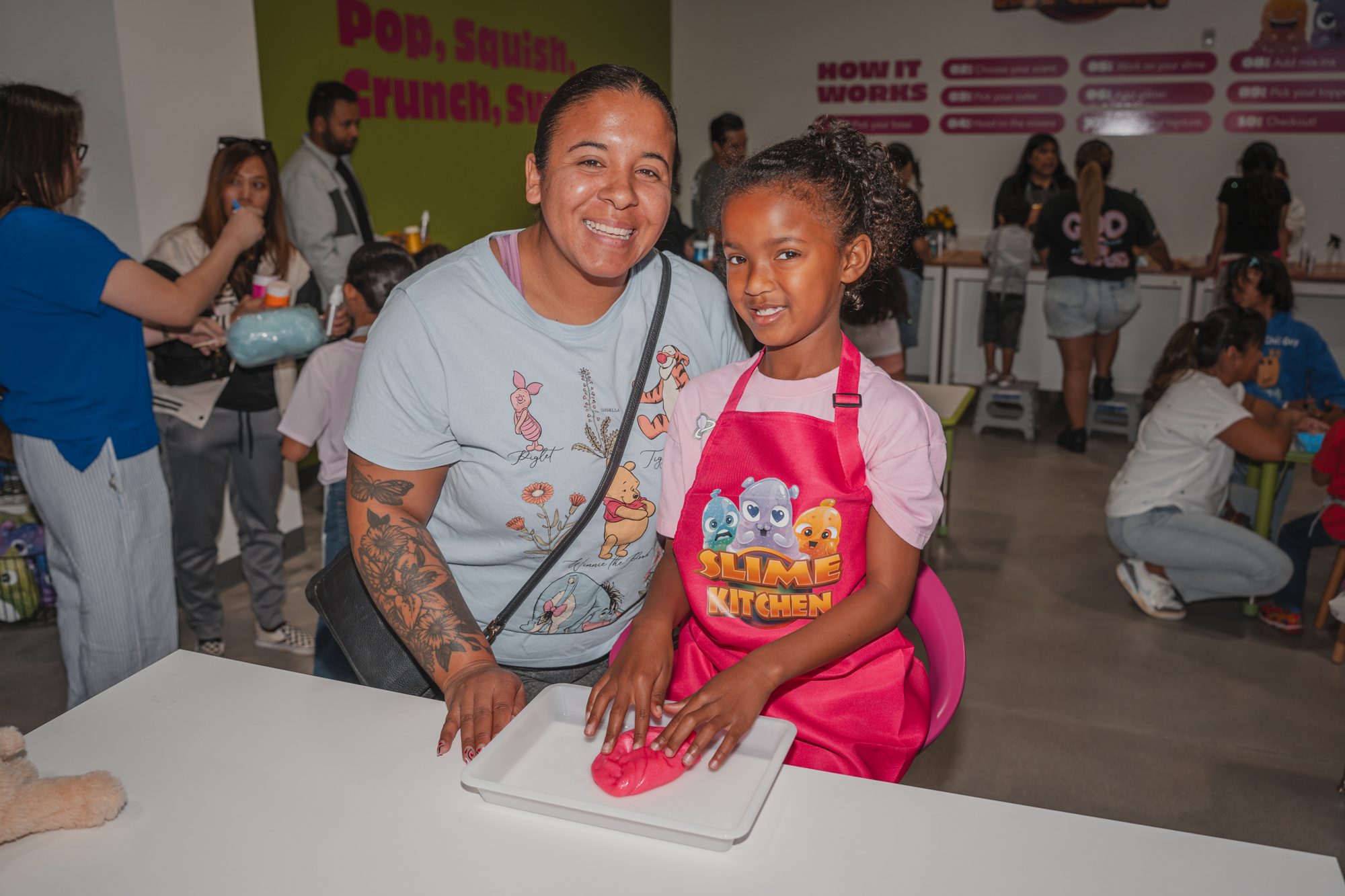 A smiling child in a Slime Kitchen apron making slime with her mom